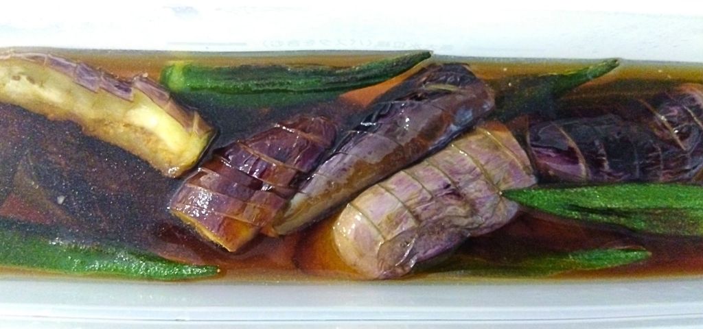 焼いたナスとおくらをタッパに入れて浸しています